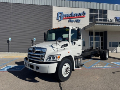 White 2025 Hino L7 cab chassis truck in showroom lot showing front and side view with Bruckner's sign in background.