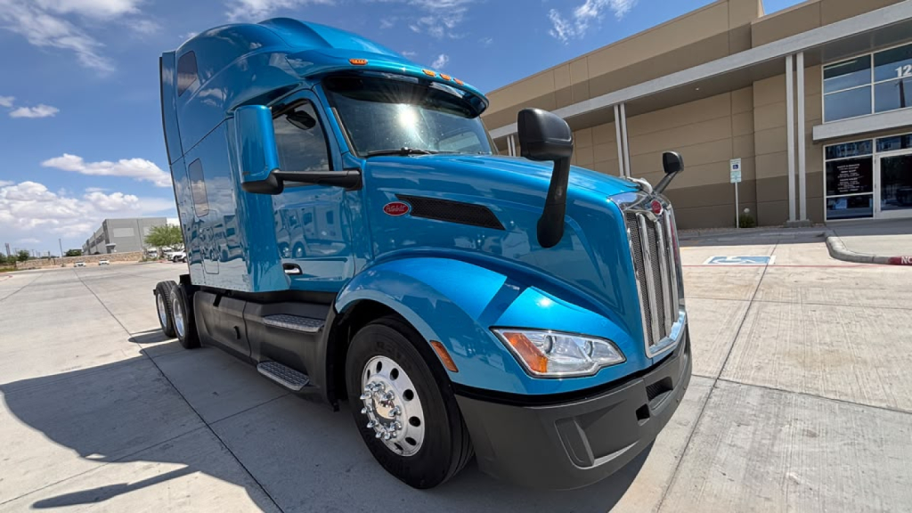 Peterbilt 579 truck in blue exterior, front-left view, showing cab, windshield, and headlights.