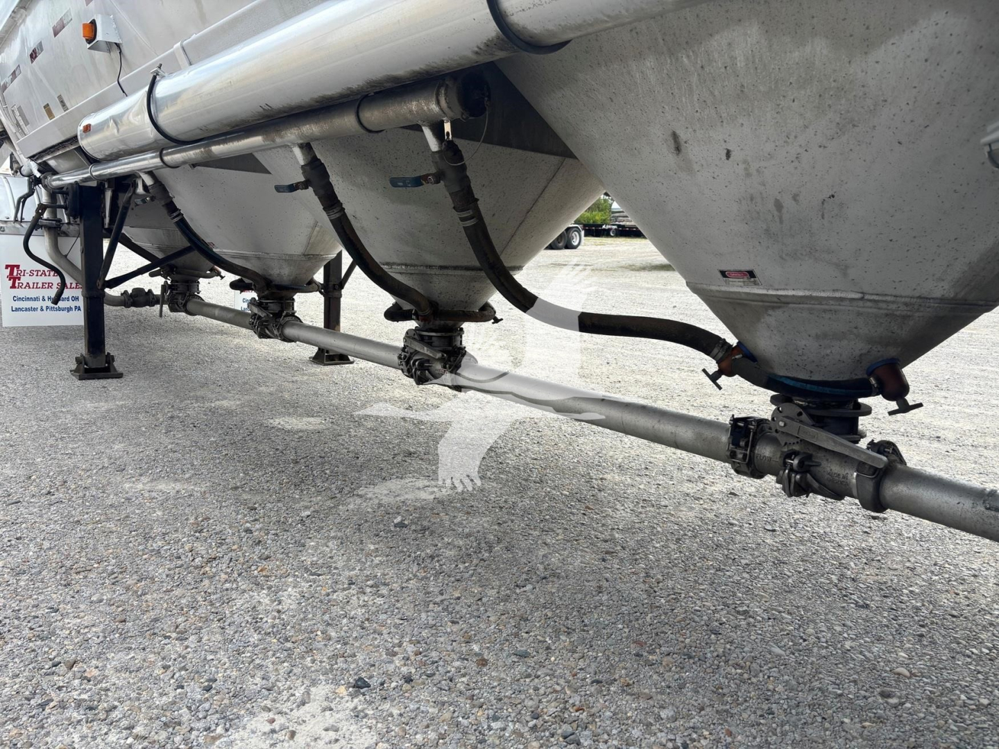 Pneumatic trailer undercarriage showing connection piping and fittings near twin hopper bottoms.