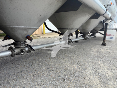 Trailer undercarriage showing multiple conical hoppers and a pneumatic piping run along the bottom with clamps and support legs.