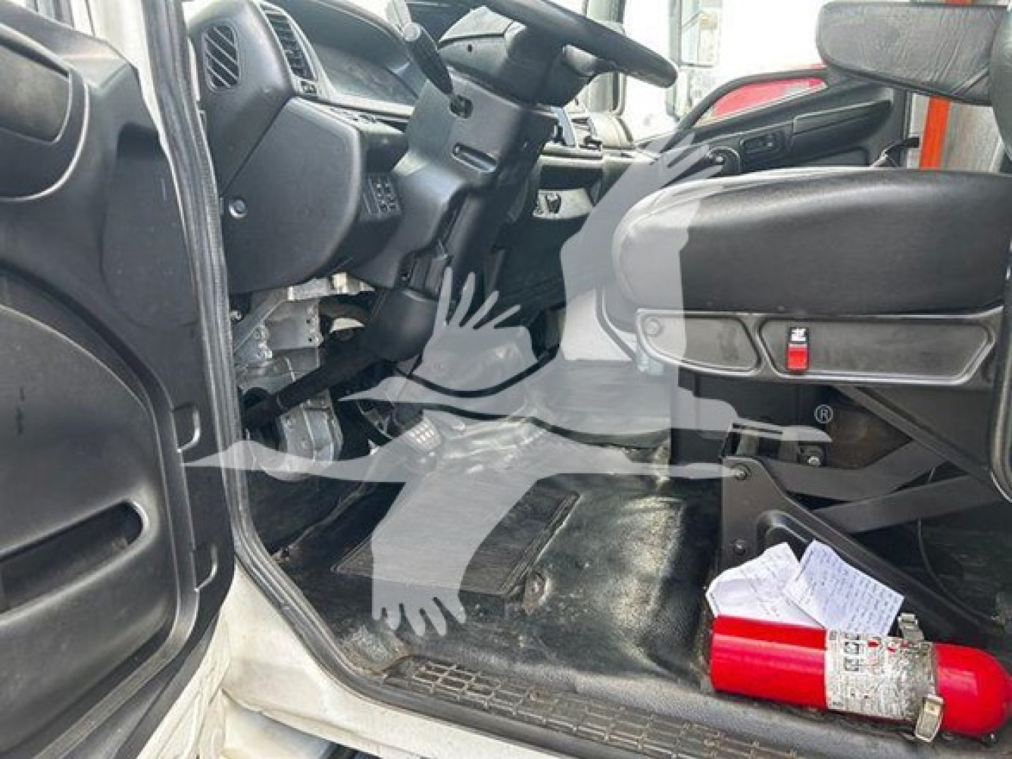 Interior of a 2020 Hino 268A cab showing driver's seat, steering wheel, pedals, and floor with a fire extinguisher and paperwork on the floor.