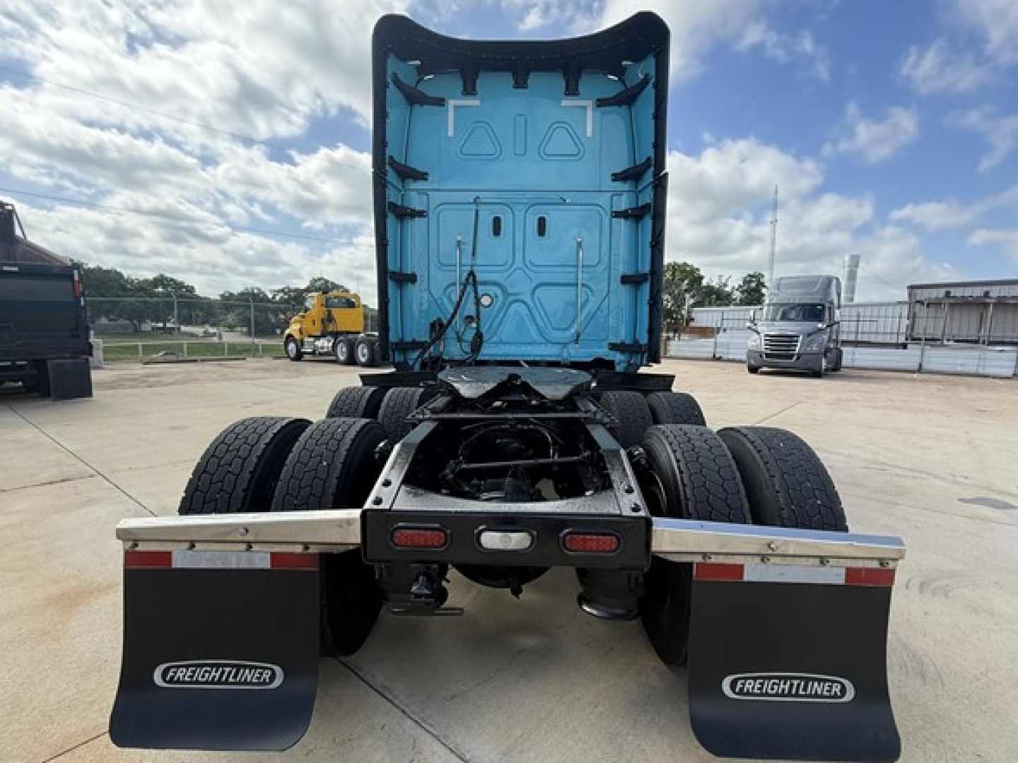 Freightliner Cascadia 126 tractor viewed from rear with blue sleeper cabin interior visible, dual rear axles, and mud flaps labeled Freightliner.