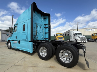 Truck cab and chassis showing Freightliner Cascadia 126 with teal cab, dual rear axles, and exposed engine bay area behind the cab