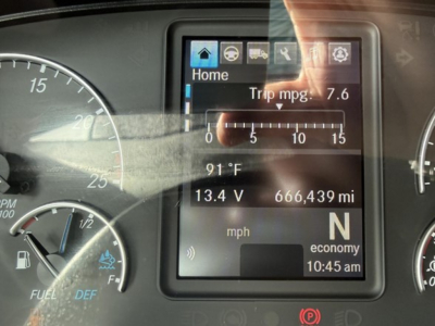 Dashboard display showing trip mpg 7.6, 91°F, 13.4 V, 666,439 miles, speedometer and fuel gauges in a Freightliner Cascadia truck cockpit.