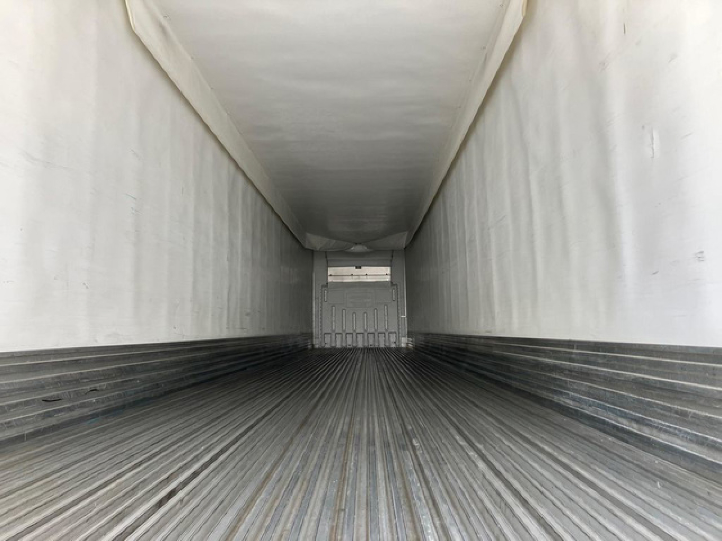 Trailer interior showing empty refrigerated trailer with ribbed metal floor and white walls, viewed from rear opening.