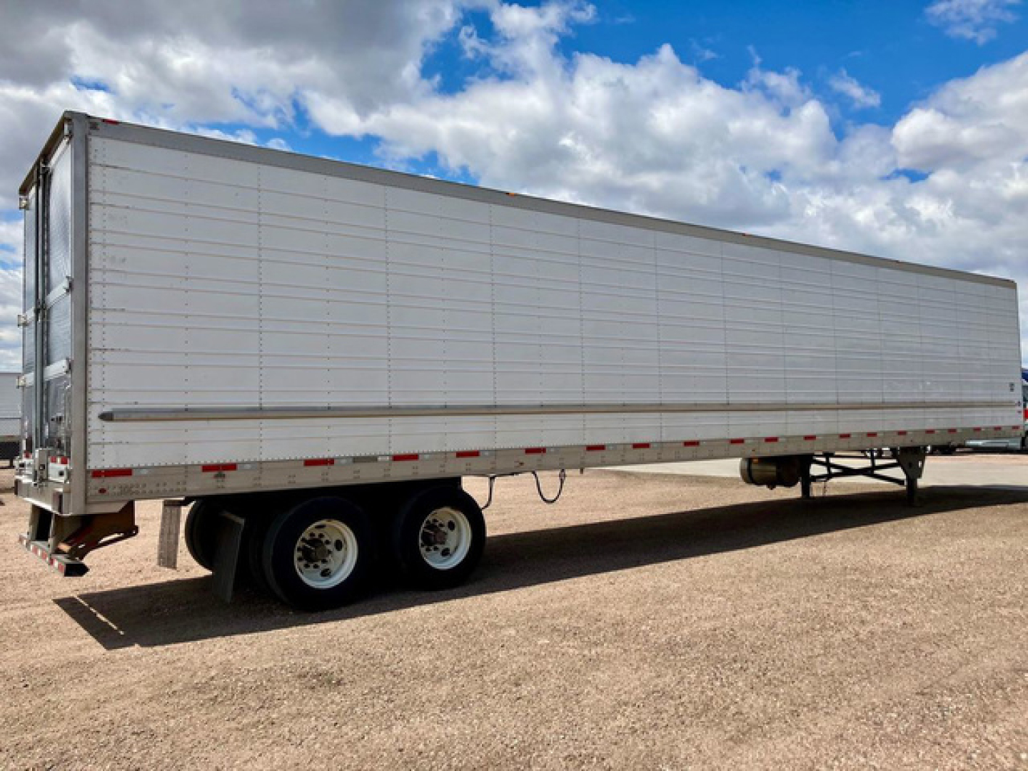 Long refrigerated trailer with dual rear axles and white insulated panels, side view under a blue sky with clouds.