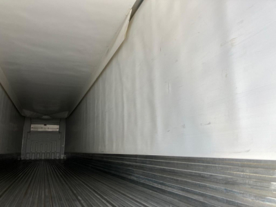 Trailer interior showing a long refrigerated cargo area with ribbed floor and side walls, empty with rear door at far end.