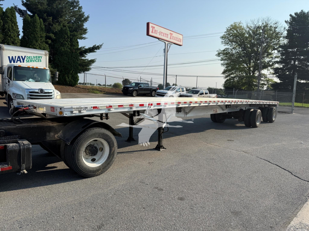 Flatbed trailer showing long aluminum deck with tandem axles and support legs, 2020 Reitnouer Maxmiser, VIN 1RNF48A28LR053393.