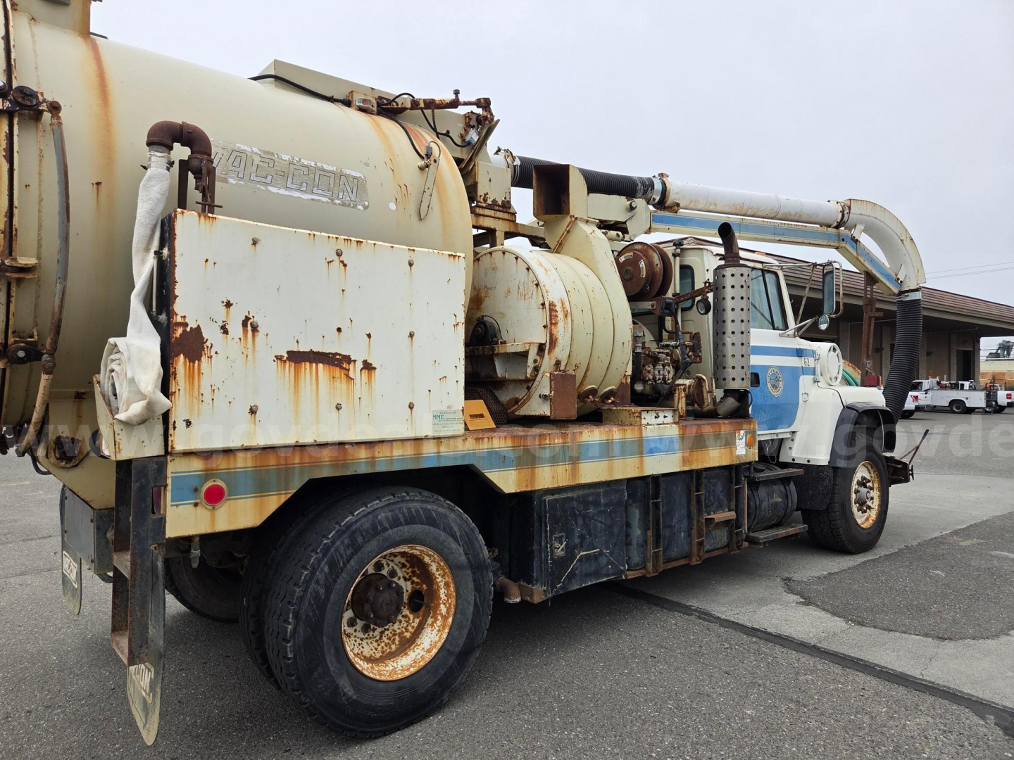 Ford LN8000 vacuum truck chassis showing large rusted tanker and hose reel with worn white cab in background.