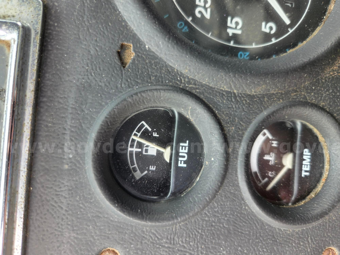 Gauge cluster and dash with fuel gauge and temperature gauge, showing 0-25 gauge markings, some rust spots, foggy lens.