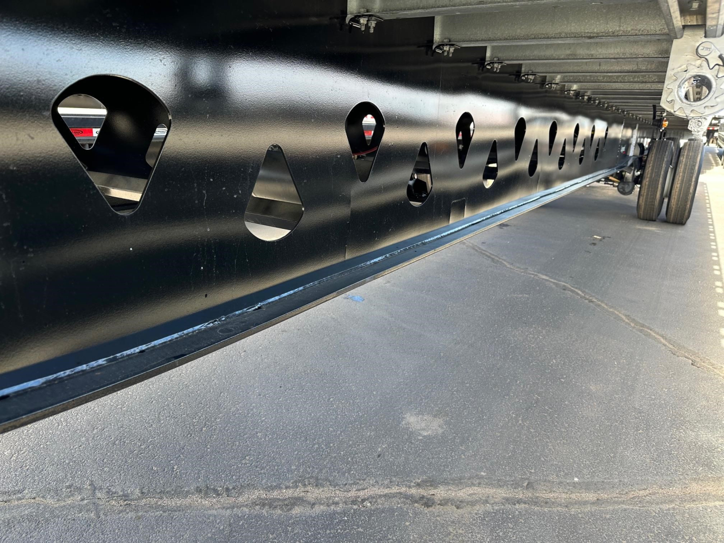 Manac 53' combo flatbed trailer side with numerous circular cutouts and trailer wheels visible at rear.