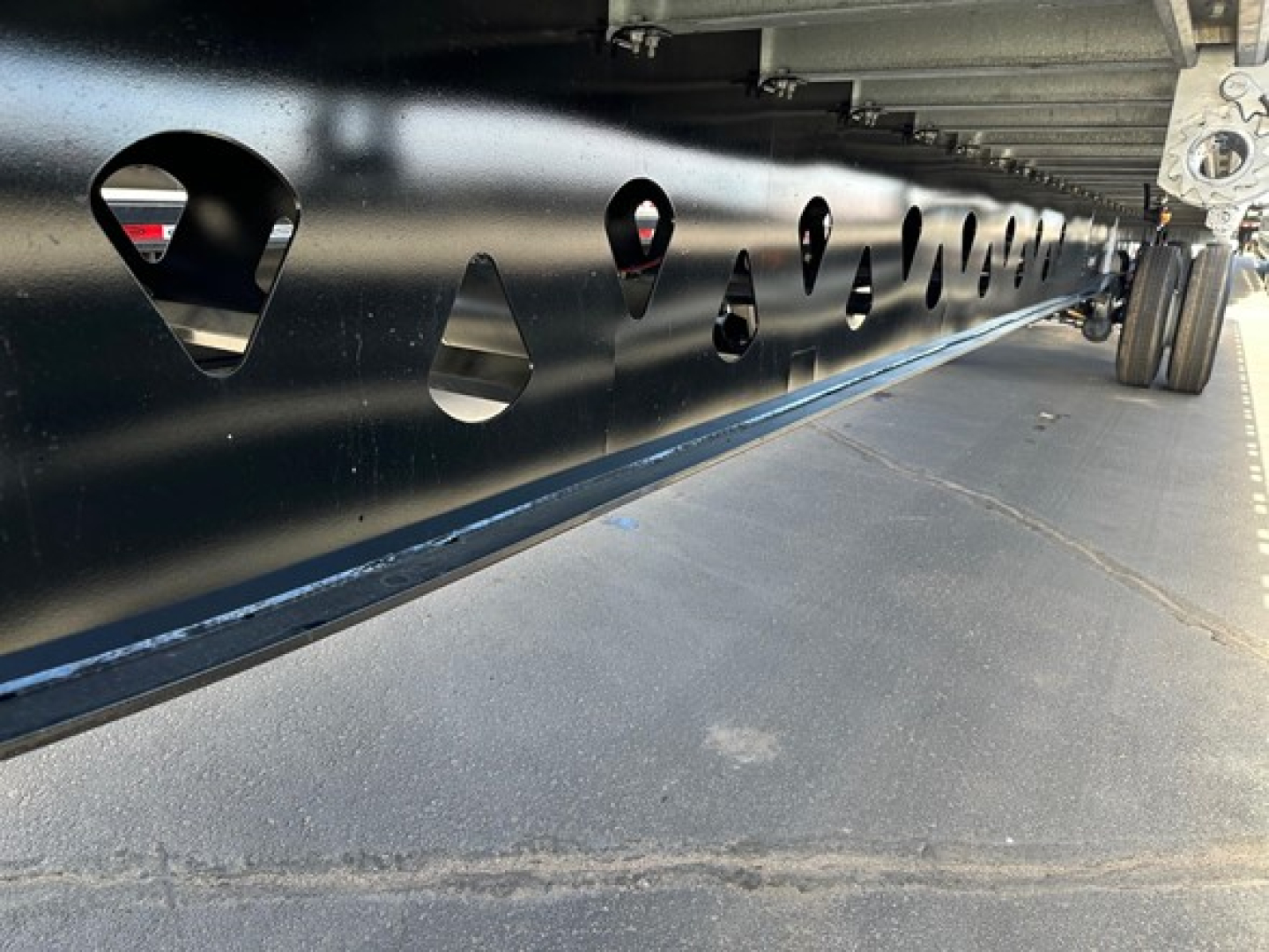 Flatbed trailer frame with series of circular cutouts and wheel for Manac Legend 2026 trailer undercarriage detail