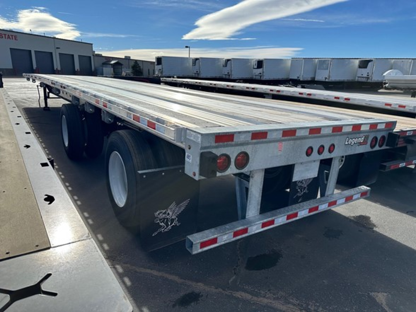 Manac Legend flatbed trailer showing dual rear axles, aluminum bed, and Legend branding at rear with taillights.