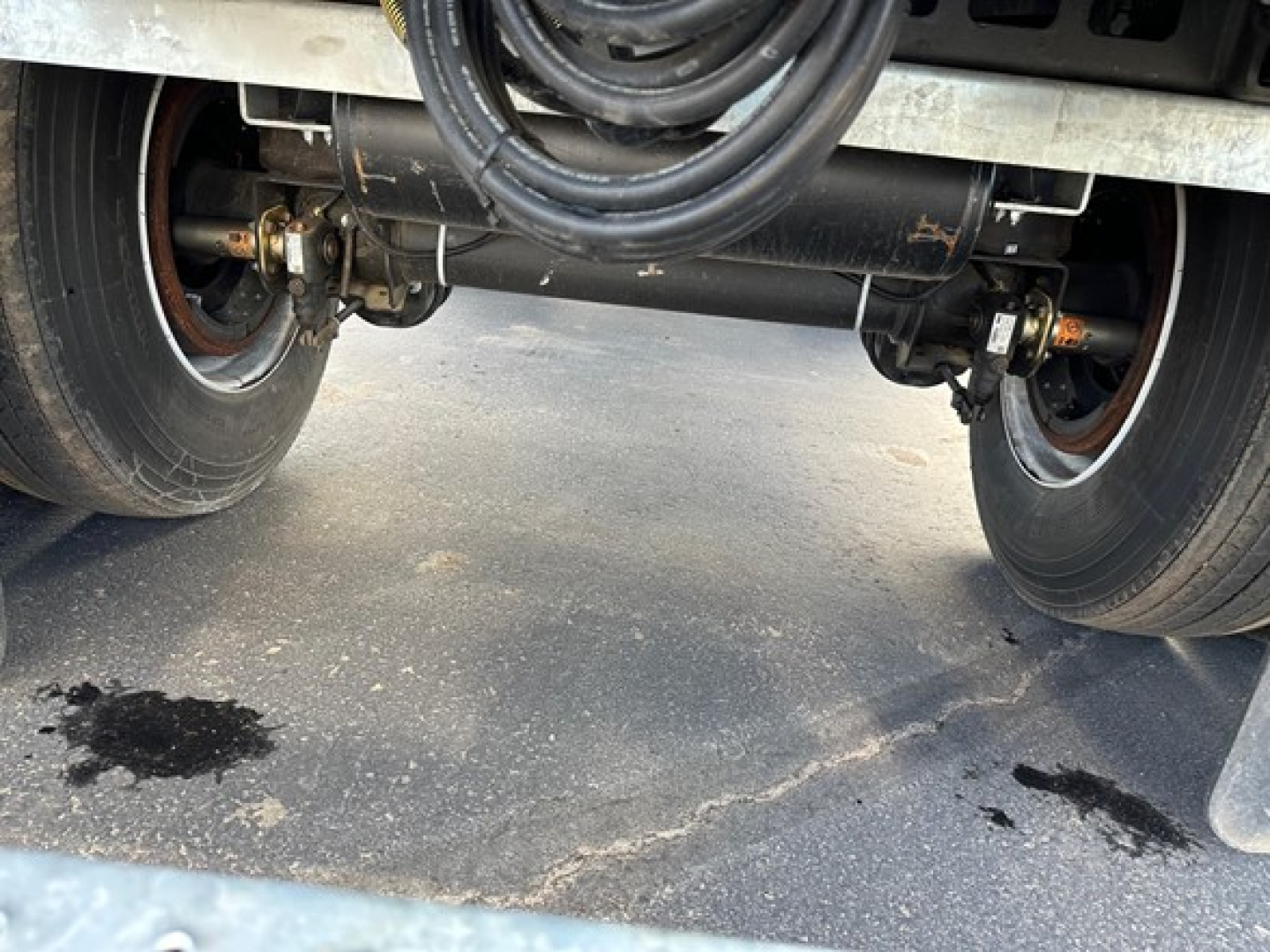 Manac Legend trailer undercarriage showing dual rear axles, suspension air lines, and braking components with tires and road surface.