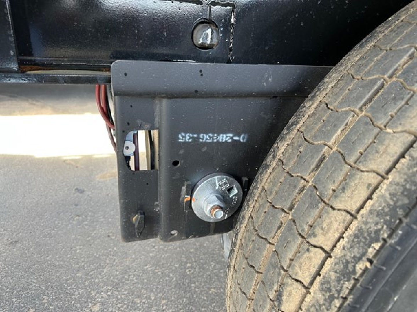Low-angle view of a Manac Legend trailer undercarriage showing a circular electrical connector port and a welded mounting plate near a front tire.