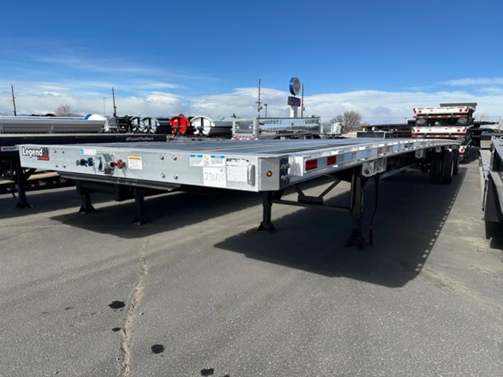 Manac Legend flatbed trailer showing beams and support legs with brand labels and stickers along the side.