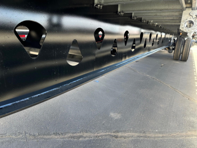 Manac 53' combo flatbed trailer side with numerous circular cutouts and trailer wheels visible at rear.