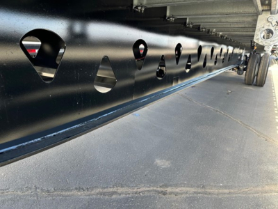 Flatbed trailer frame with series of circular cutouts and wheel for Manac Legend 2026 trailer undercarriage detail