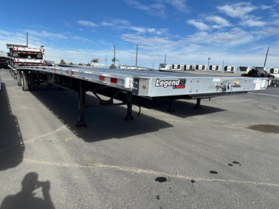 Flatbed trailer showing Legend-brand emblem and sturdy frame with landing gear, parked in lot under blue sky.