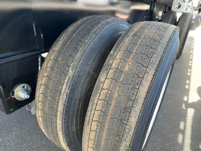 Two rear trailer tires mounted on a flatbed trailer axle, with a portion of the chassis and bolt visible.