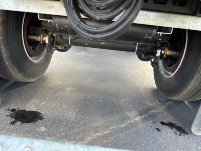 Manac Legend trailer undercarriage showing dual rear axles, suspension air lines, and braking components with tires and road surface.