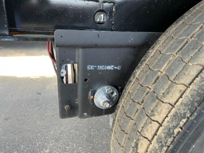 Low-angle view of a Manac Legend trailer undercarriage showing a circular electrical connector port and a welded mounting plate near a front tire.