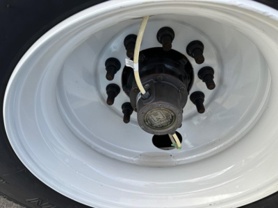 Wheel hub and lug nuts on a white trailer rim with electrical wiring harness visible.