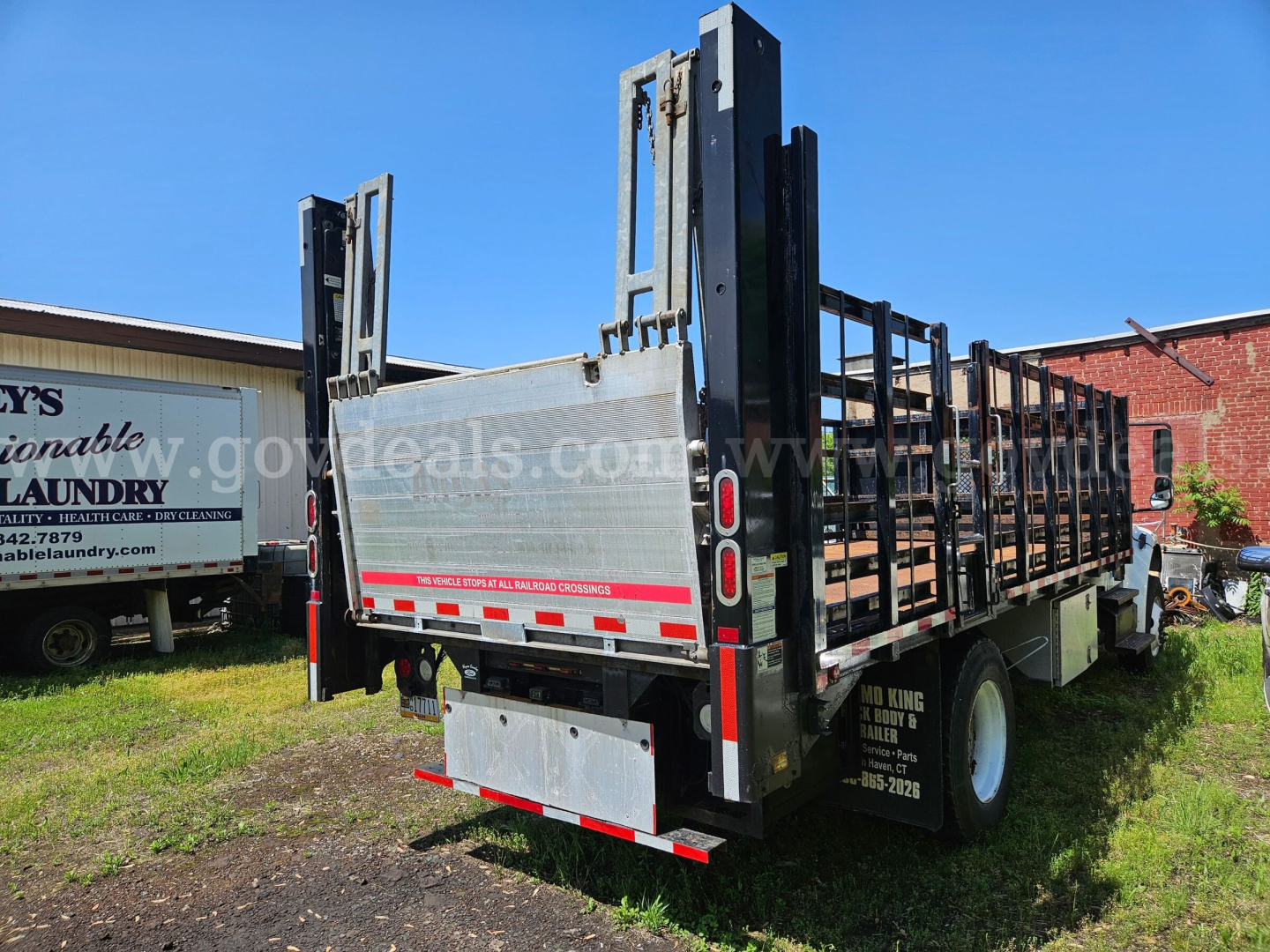 Freightliner M2-106 flatbed truck rear and side view showing steel drop-down ramps and reflective striping.