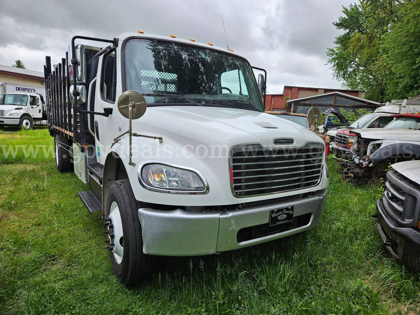 Front view of a 2013 Freightliner M2 106 flatbed truck showing cab, grille, headlights, and side mirrors.