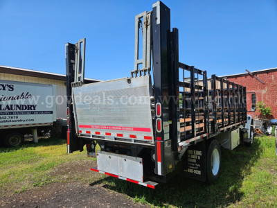 Freightliner M2-106 flatbed truck rear and side view showing steel drop-down ramps and reflective striping.