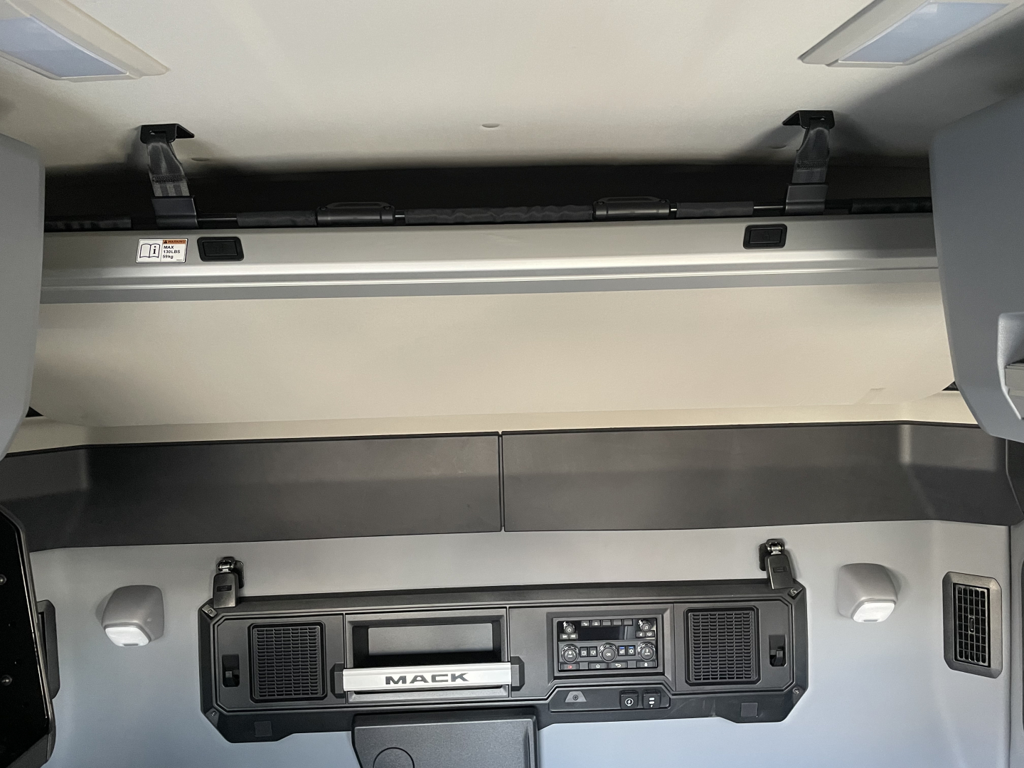 Mack PR64T64 truck cab interior showing dashboard center with control panel and storage compartments; faint view of sleeper area overhead console.
