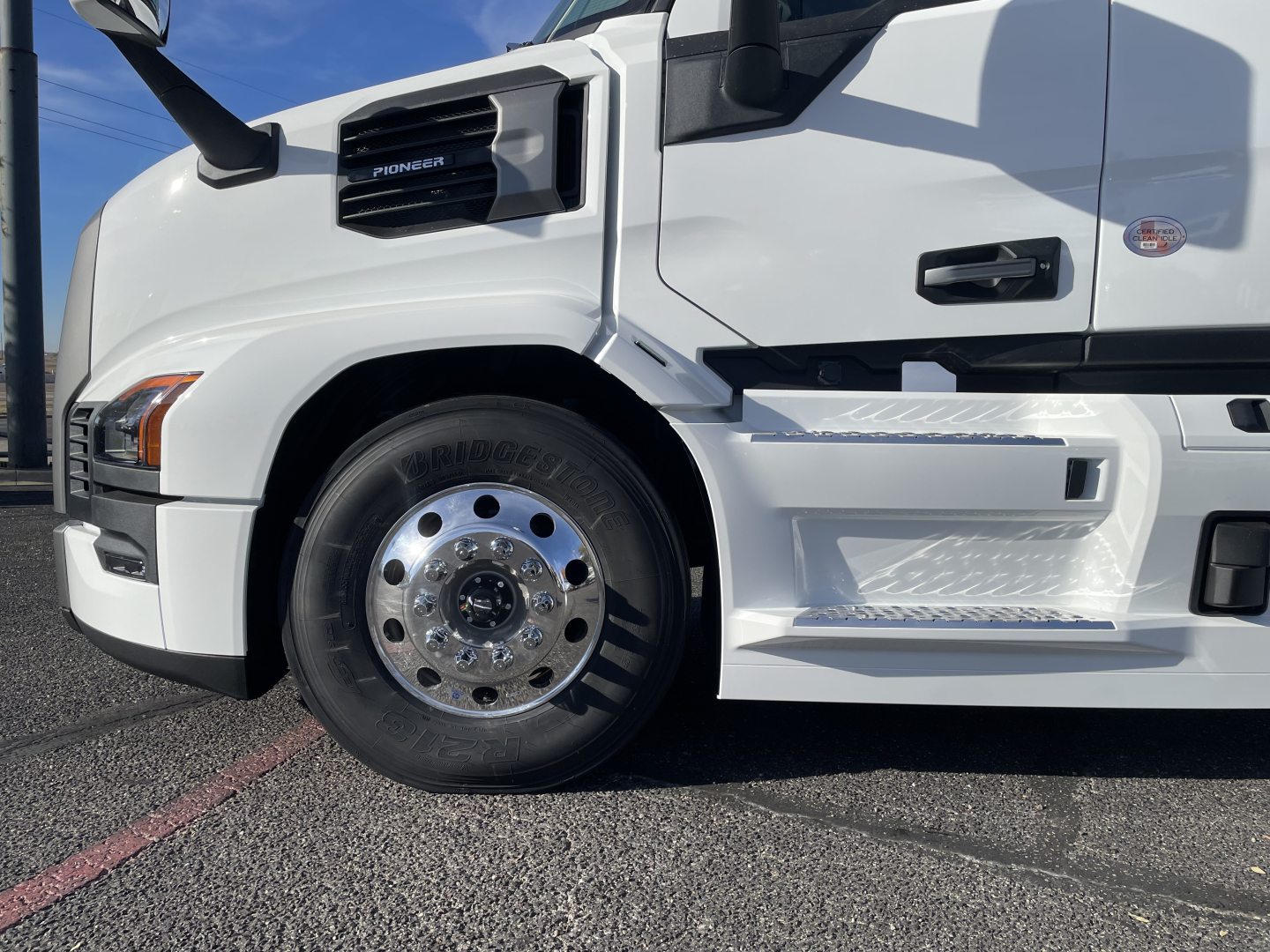 Front left side of a white Mack PR64T64 truck showing front wheel, chrome hubcap, and steps with textured surface.
