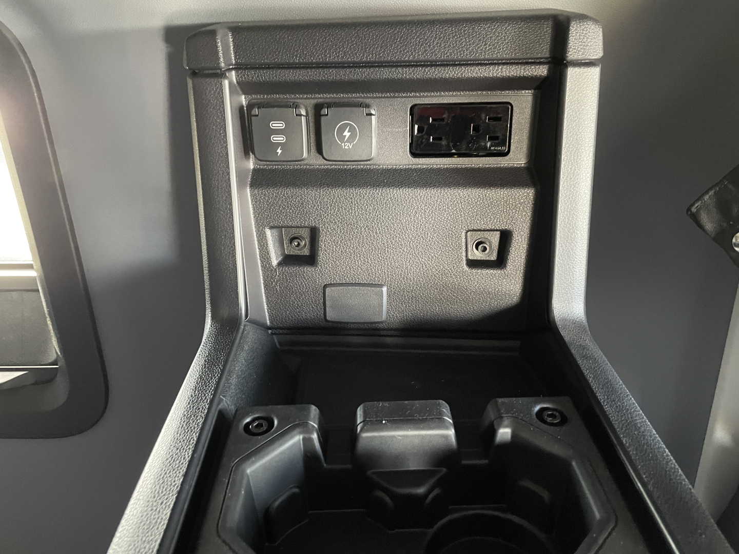 Truck interior center console with power outlet, USB/12V ports, and ethernet-like connector visible; storage cubby and cup holder area in view.