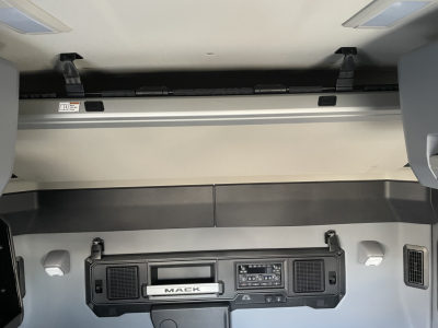 Mack PR64T64 truck cab interior showing dashboard center with control panel and storage compartments; faint view of sleeper area overhead console.