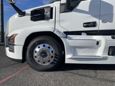 Front left side of a white Mack PR64T64 truck showing front wheel, chrome hubcap, and steps with textured surface.