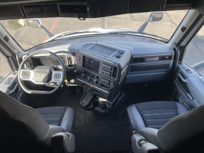 Interior of a Mack PR64T64 cab showing steering wheel, dashboard with digital displays, center console, and two front seats.