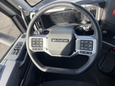 Steering wheel of a new Mack PR64T64 truck interior with controls on both sides and Mack logo in center.