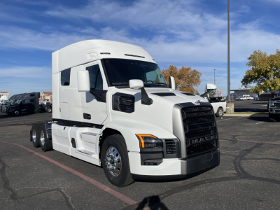 2026 Mack PR64T64 truck tractor in a dealership lot, white exterior, highway-king-style grille, large side mirrors, and dual rear axles visible.