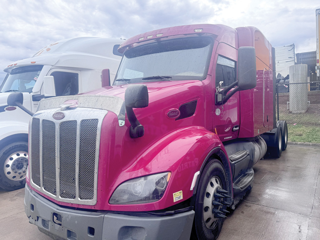 Peterbilt 579 UltraCab tractor in magenta/pink, front grille, large chrome bumper, side mirrors, dual rear wheels, daytime running lights, aerodynamic sleeper cabin.