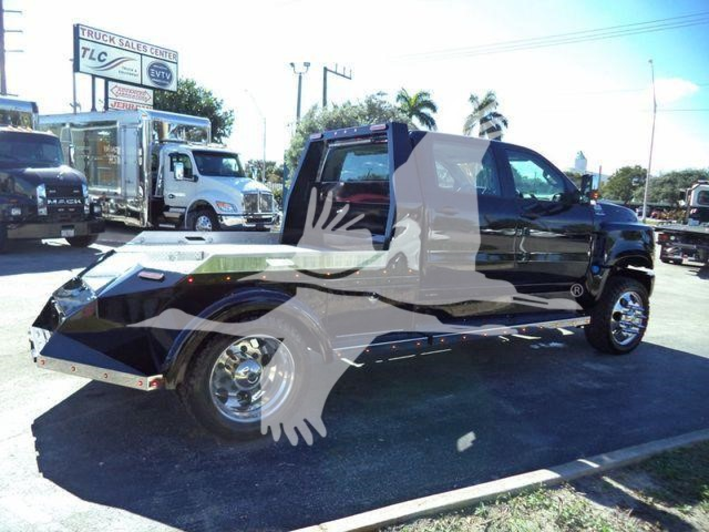 Truck with stretched cab and large flatbed trailer hitch on a dealership lot; multiple trucks visible in background.