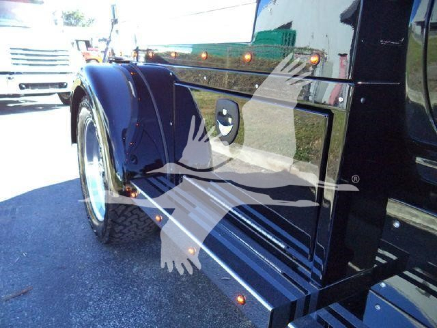 Truck fender and side panel with chrome trim, blue paint, and wheel well, reflecting sunglasses logo watermark overlay.
