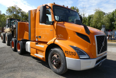 Volvo VNR64T300 conventional daycab truck showing front and side with orange cab and black accents.