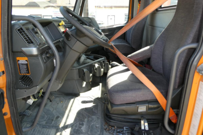  Volvo VNR64T300 daycab interior with steering wheel, dashboard, and driver's seat showing seating belt and pedals.