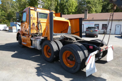 Orange Volvo VNR64T300 daycab truck chassis rear view showing twin rear axles and chain hoist attachments.