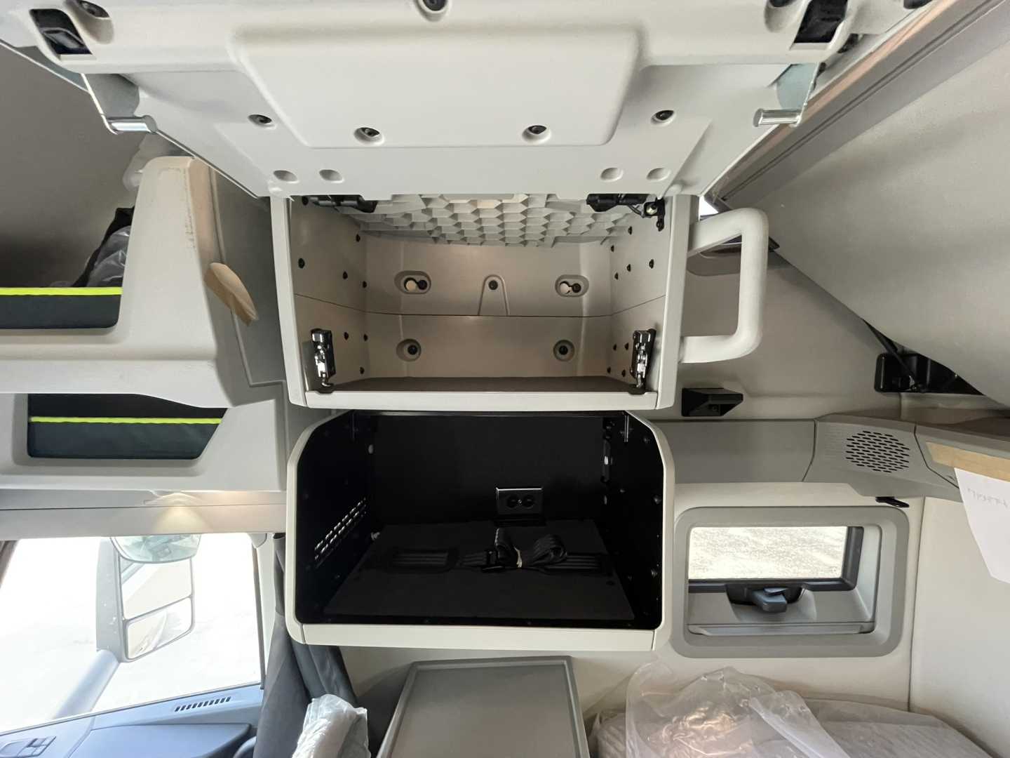 Cab interior showing front storage compartment and dashboard area of a 2026 Volvo VNL64T860 sleeper with open overhead box and small console gap.