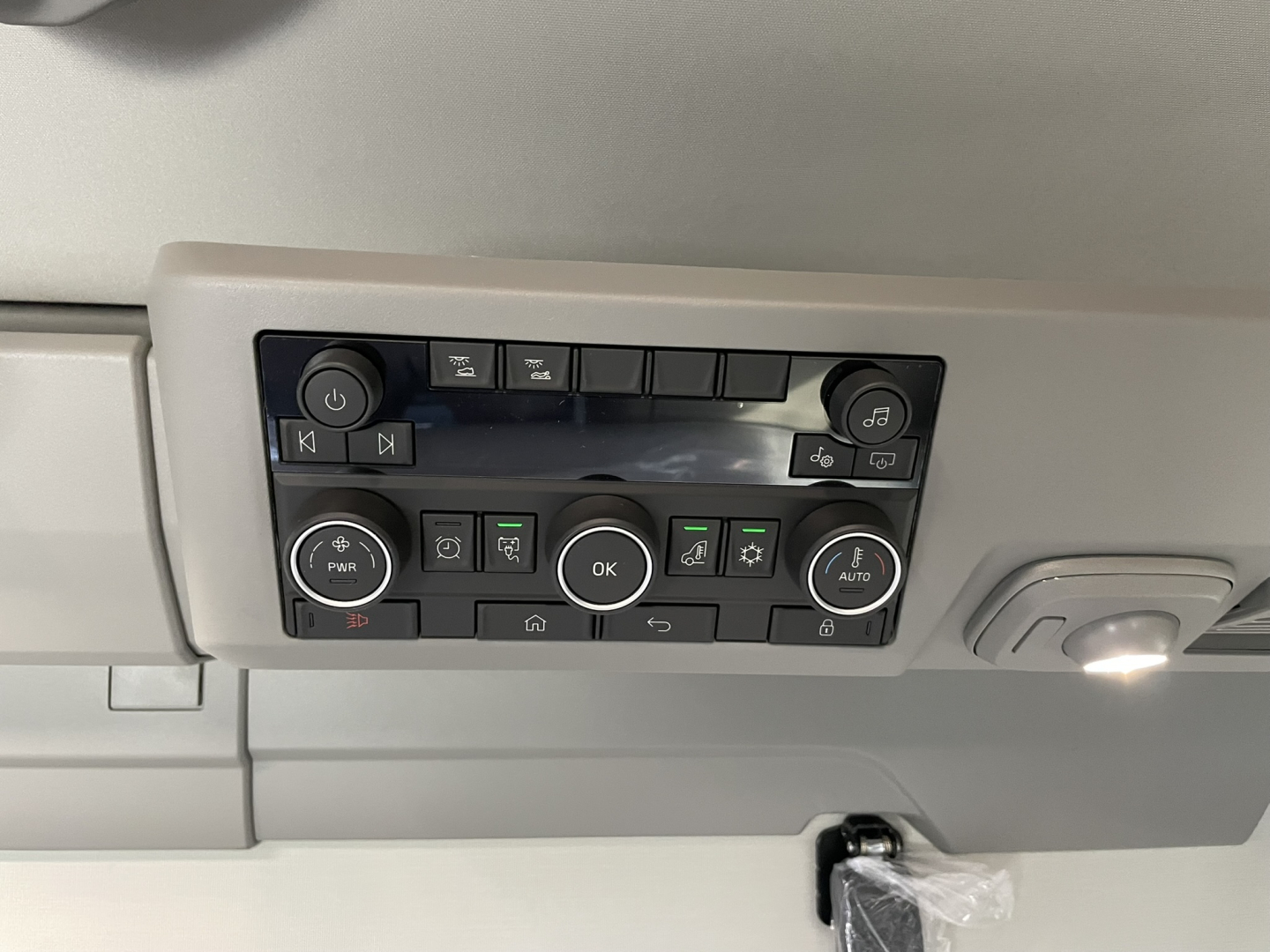 Volvo truck interior overhead control panel with multiple buttons and circular knob, dash lighting, and cockpit light; center console buttons visible.