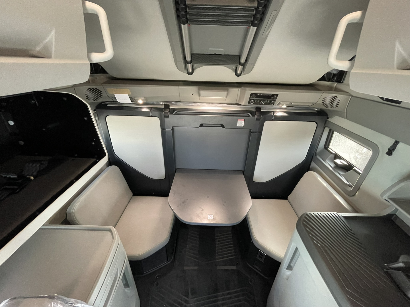Volvo VNL64T860 sleeper cab interior showing front-facing seating area with table and overhead storage panels.