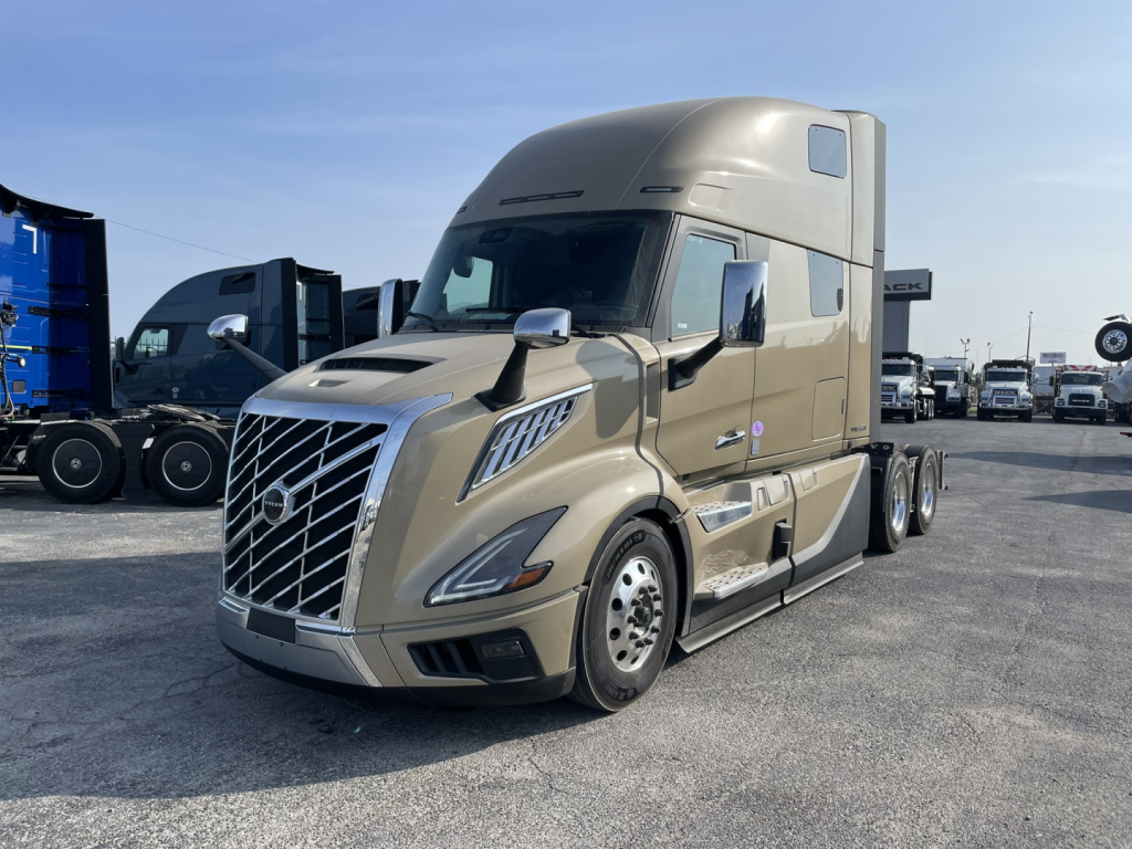 Volvo VNL64T860 sleeper cab tractor showing front grille and side view with chrome mirrors and tan paint.