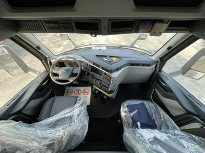 Volvo VNL64T860 truck cab interior showing steering wheel, dashboard controls, and plastic-wrapped seats, front view from driver seat.