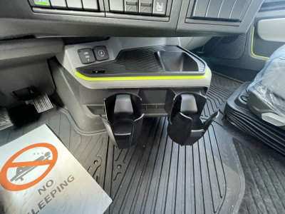 Volvo VNL interior center console with cupholders and storage area; prominent lime-green accent line above the pedals, floor mats, and a no-sleeping placard on the floor.